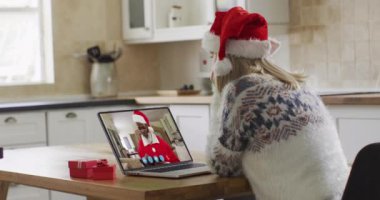 Laptop görüntülü sohbetinde Noel Baba şapkası takan beyaz bir kadın. Covid 19 salgını sırasında aile ve arkadaşlarla iletişim kurmak.