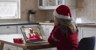 Laptop görüntülü sohbetinde Noel Baba şapkası takan beyaz bir kadın. Covid 19 salgını sırasında aile ve arkadaşlarla iletişim kurmak.