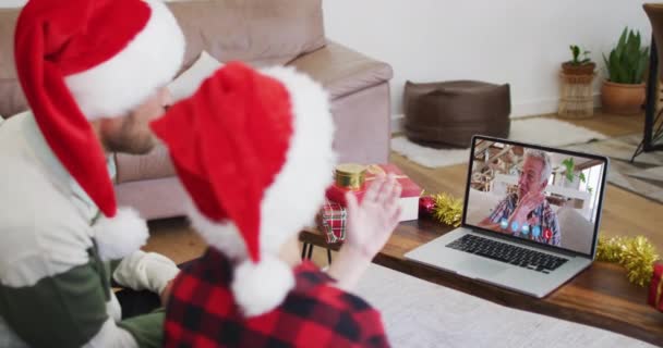 自宅でクリスマスの間 ノートパソコンのビデオチャットでサンタの帽子をかぶっている白人の父と息子 19大流行期のクリスマスに友人や家族とのコミュニケーションは — ストック動画