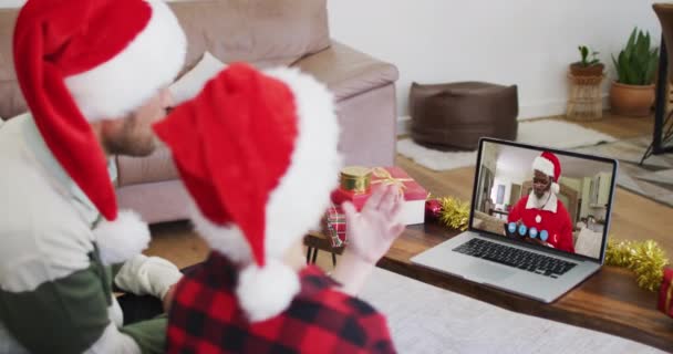 自宅でクリスマスの間にラップトップビデオチャットでサンタの帽子をかぶっている息子を持つ白人男性 19大流行期のクリスマスに友人や家族とのコミュニケーションは — ストック動画