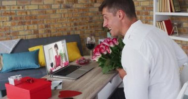 Sevgililer gününde çeşitli çiftler ellerinde çiçek ve dizüstü bilgisayar ekranında kadın olan video görüşmeleri yapıyorlar.