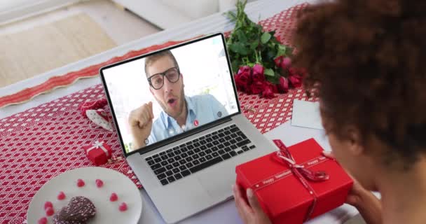 Diversa pareja en una fecha de San Valentín videollamada hombre en la pantalla hablando con la mujer regalo de apertura — Vídeos de Stock