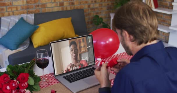 Diversa pareja en una fecha de San Valentín videollamada hombre mostrando anillo a la mujer sonriente en la pantalla del ordenador portátil — Vídeos de Stock