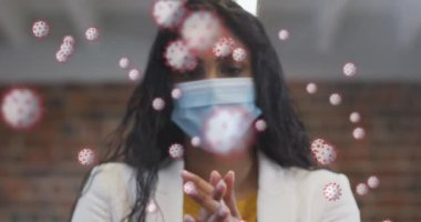 Ofiste yüz maskesi takan melez bir kadının portresinin üzerinde yüzen kovid 19 hücrenin animasyonu. Coronavirus covid 19 salgını sırasında sağlık ve korunma, dijital olarak üretilen video.