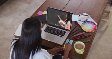 Beyaz kız öğrenci, bayan öğretmenle video görüşmesinde dizüstü bilgisayar kullanıyor, notlar alıyor. Çevrimiçi eğitim karantina süresince evde tek başına kalıyor..