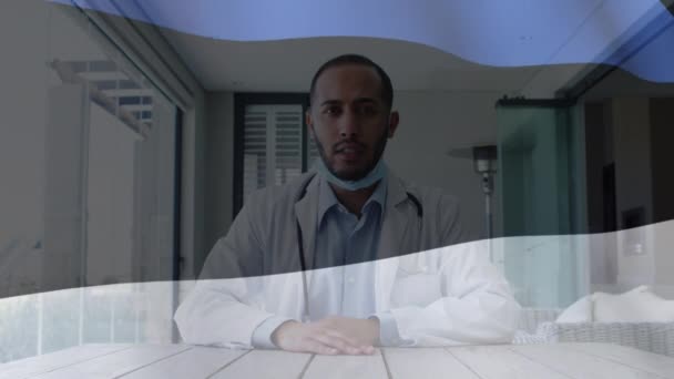 在办公桌前与戴面具的男医生一起为雌雄同体的旗帜动画 提供视频咨询 Coronavirus Covid 19大流行病期间的保健和保护 数码录像 — 图库视频影像