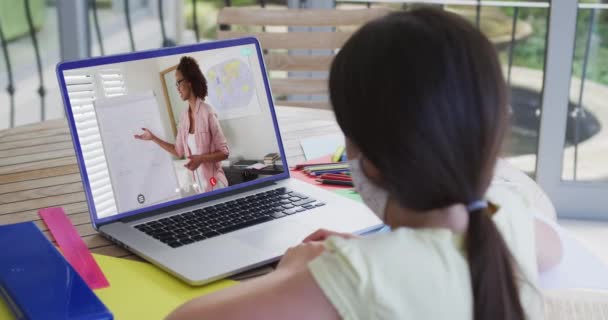 女性教師とのビデオ通話でラップトップを使用して顔マスク中の白人女子高生 隔離中に自宅に隔離されているオンライン教育 — ストック動画