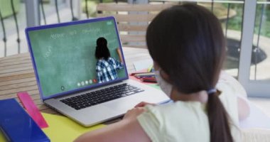 Kadın öğretmenle görüntülü görüşmede dizüstü bilgisayar kullanan maskeli beyaz bir öğrenci. Çevrimiçi eğitim karantina süresince evde tek başına kalıyor..