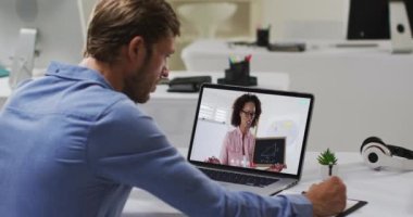 Beyaz erkek öğrenci, bayan öğretmenle video görüşmesinde dizüstü bilgisayar kullanıyor, notlar alıyor. Çevrimiçi eğitim karantina süresince evde tek başına kalıyor..
