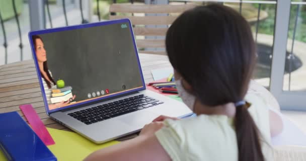 女性教師とのビデオ通話でラップトップを使用して顔マスク中の白人女子高生 隔離中に自宅に隔離されているオンライン教育 — ストック動画