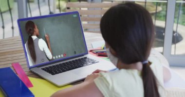 Kadın öğretmenle görüntülü görüşmede dizüstü bilgisayar kullanan maskeli beyaz bir öğrenci. Çevrimiçi eğitim karantina süresince evde tek başına kalıyor..