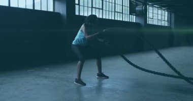 Terk edilmiş bir binada iplerle egzersiz yapan bir kadının üzerinde süzülen parlak ışığın animasyonu. Dijital arayüz küresel spor ve performans konsepti dijital olarak oluşturulmuş video.