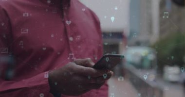 Şehirde akıllı telefon kullanan Afro-Amerikan bir adam üzerinde dijital simgelerle ağ animasyonları. küresel sosyal ağ, iletişim ve bağlantı konsepti dijital olarak oluşturulmuş video.