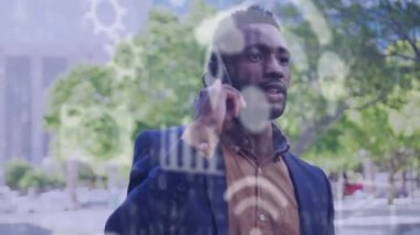 Sokakta akıllı telefondan konuşan Afro-Amerikan bir adama karşı yüzen birden fazla dijital ikon. küresel ağ ve teknoloji kavramı