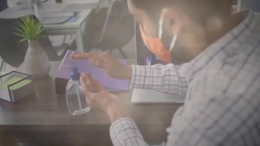 Ofiste ellerini sterilize eden yüz maskesi takan adama karşı ışık. Coronavirus covid 19 salgını sırasında işyerinde hijyen ve sosyal mesafeler