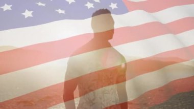 Sahilde dikilen Afro-Amerikan adamın üzerinde Amerikan bayrağının dalgalanması. ABD vatanseverliği ve demokrasi kavramı dijital olarak üretilmiş video. Amerikan erkeği.