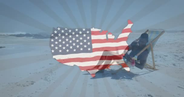 ビーチのデッキチェアで飲んでいる男に手を振るアメリカの旗の地図のアニメーション アメリカの愛国心と民主主義の概念をデジタルで — ストック動画