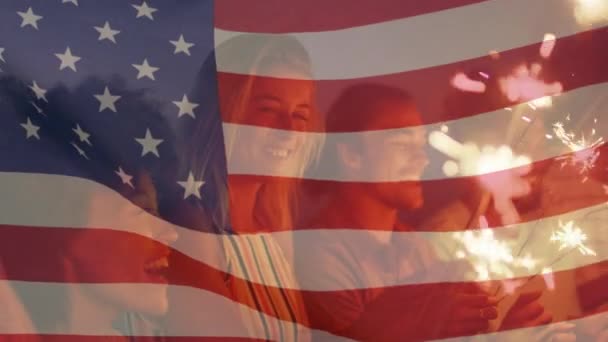 Animation einer amerikanischen Flagge, die über einer Gruppe von Freunden weht, die Wunderkerzen am Strand halten — Stockvideo