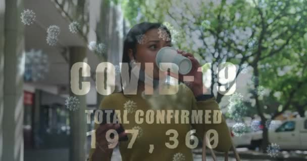 Текст Covid-19 зі збільшенням кількості проти жінки, що п'є каву та використовує смартфон — стокове відео