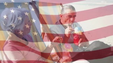 Amerikan bayrağının kumsalda içki içen yaşlı çift üzerinde dalgalanması. ABD vatanseverliği ve demokrasi kavramı dijital olarak oluşturulmuş video.