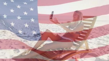 Amerikan bayrağının kumsalda akıllı telefon kullanarak selfie çektiği bir sahne. ABD vatanseverliği ve demokrasi kavramı dijital olarak oluşturulmuş video.