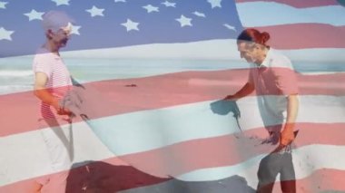 Sahile battaniye seren yaşlı bir çiftin üzerinde Amerikan bayrağının dalgalanması. ABD vatanseverliği ve demokrasi kavramı dijital olarak oluşturulmuş video.