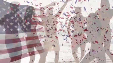 Amerikan bayrağının dalgalanması ve kumsalda dans eden arkadaşlarının üzerine konfeti. ABD vatanseverliği ve kutlama konsepti dijital olarak oluşturulmuş video.