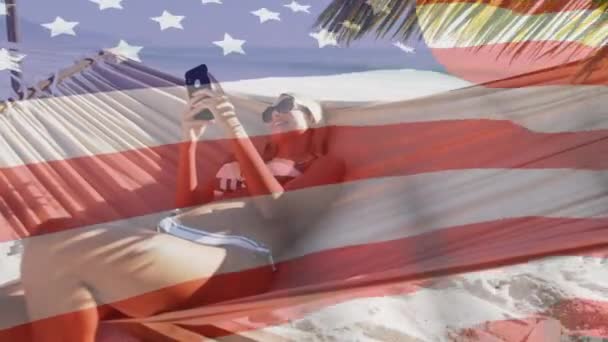 Animación Bandera Americana Ondeando Sobre Mujer Hamaca Usando Smartphone Playa — Vídeos de Stock