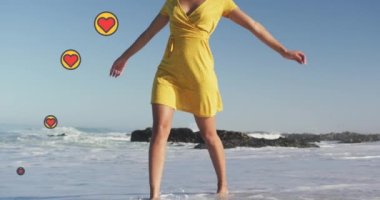 Animation of heart digital icons over woman dancing on beach. digital interface, social media and global technology concept digitally generated video.