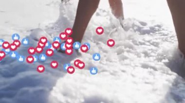 Heart and like icons floating against low section of couple walking in the water on the beach. social media networking and vacation concept