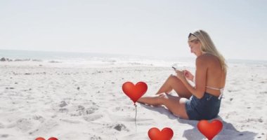 Animation of red heart love balloons digital icons over woman using smartphone on beach. digital interface, social media and global networking concept digitally generated video.
