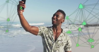 Animation of spinning networks with social media digital icons over man using smartphone on beach. digital interface, social media and global networking concept digitally generated video.