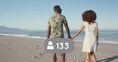 Profile icons with increasing numbers against african american couple walking on the beach. social media networking and vacation concept