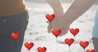 Animation of red heart love balloons digital icons over couple holding hands on beach. digital interface, social media and global networking concept digitally generated video.