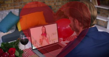 Dizüstü bilgisayarda video görüşmesi yaparken beyaz bir adamın el sallamasının ardından birleşik kırmızı kalpler oluşuyor. Sevgililer Günü 'nün uzak kutlaması online ve flört konsepti