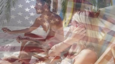 Sahilde güverte sandalyesinde oturan beyaz çifte karşı Amerikan bayrağı sallanıyor. Amerika 'nın bağımsızlığı vatansever tatil konsepti