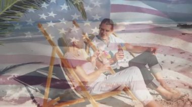 Amerikan bayrağı, kumsaldaki iskemlede oturup içkinin keyfini çıkaran yaşlı çifte karşı sallanıyor. Amerika 'nın bağımsızlığı vatansever tatil konsepti