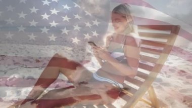 Kumsalda güverte sandalyesinde oturan beyaz bir kadına Amerikan bayrağı sallıyor. Amerika 'nın bağımsızlığı vatansever tatil konsepti