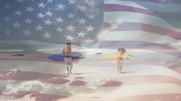 Американский Флаг Размахивающий Против Африканской Американской Пары Досками Серфинга Пляже — стоковое видео