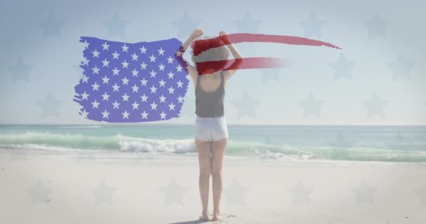 美国国旗向站在海滩上张开双臂的非洲裔美国女人飘扬 美国独立爱国假日的概念 — 图库视频影像
