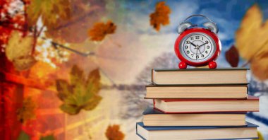 Bir yığın kitabın üzerinde duran bir çalar saat. Arka planda sonbahar yaprakları ve kış manzarası var. okul konseptine geri dön.