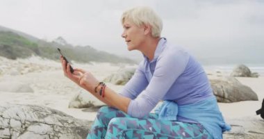 Akıllı telefon kullanarak deniz kenarındaki yaşlı kadın üzerinde dijital insan simgeleri oluşturuluyor. küresel sosyal medya ve dijital arayüz konsepti dijital olarak oluşturulmuş video.