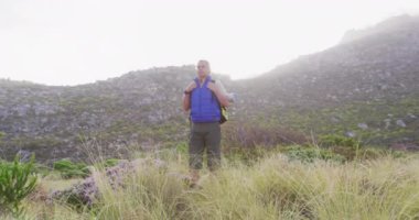 Kafkas kıdemli bir adam kırsalda yürüyüş yapıyor, hızlı hareket eden bulutların üzerinde. aktif yaşam tarzı, sağlıklı emeklilik ve özgürlük konsepti, dijital olarak oluşturulmuş video.