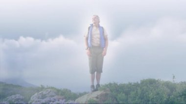 Kafkas kıdemli adam kırsalda yürüyüş yapıyor, kollarını açıyor, hızlı hareket eden bulutların üzerinde. aktif yaşam tarzı, sağlıklı emeklilik ve özgürlük konsepti, dijital olarak oluşturulmuş video.