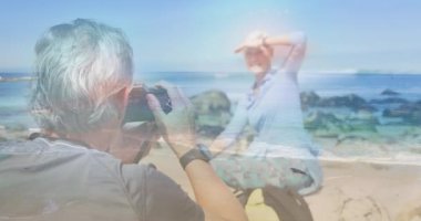 Deniz dalgaları üzerinde fotoğraf çeken mutlu beyaz bir çift. etkin emeklilik yaşam tarzı konsepti dijital olarak oluşturulmuş video.