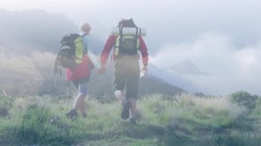 Hızlı hareket eden bulutların üzerinde dağlarda yürüyüş yapan Kafkasyalı mutlu çift. etkin emeklilik yaşam tarzı konsepti dijital olarak oluşturulmuş video.