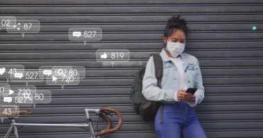 Sosyal medya simgelerinin animasyonu ve akıllı telefon kullanan yüz maskeli kadın üzerindeki afişler. küresel covid 19 salgın, teknoloji ve dijital arayüz konsepti dijital olarak oluşturulmuş video.