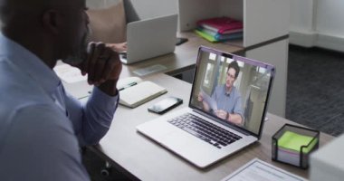 Afrika kökenli Amerikalı üst düzey bir adam, erkek ofis arkadaşı ile laptopta video görüşmesi yapıyor. iş, profesyonellik ve teknoloji kavramı