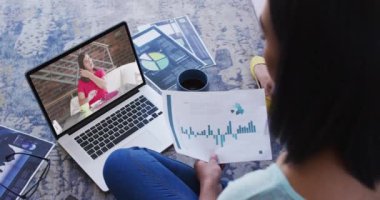 Afro-Amerikalı bir kadın elinde bir belge tutuyordu ve evdeki bilgisayarından bir video görüşmesi yapıyordu. ev kavramından çalışmak