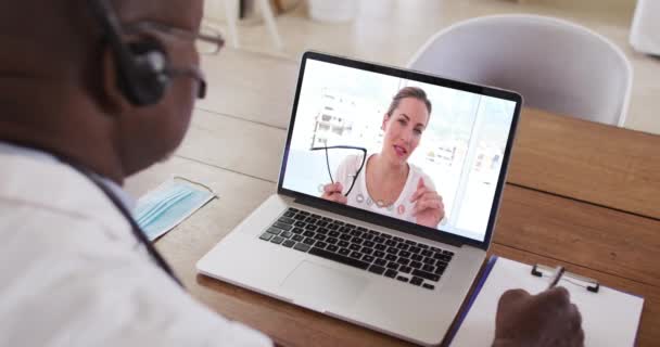 Médico Afroamericano Con Auriculares Tomando Notas Mientras Hace Una Videollamada — Vídeo de stock